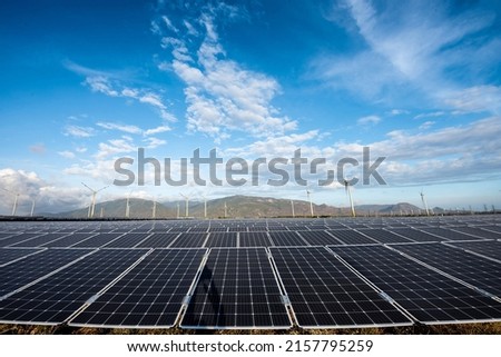 Solar panes in a solar park used for clean energy production. Solar panel under blue sky with sun. Green grass and cloudy sky. Alternative energy concept to reduce global warming and climate change