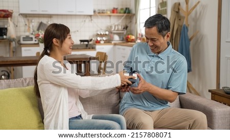 asian Japanese adult daughter showing her father a gift from behind on Father’s Day at home. surprised elderly man saying thanks to her sweet act