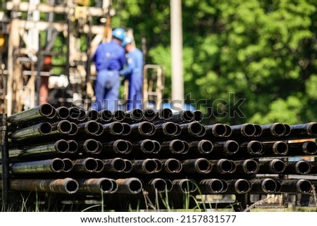 Oil rig drill pipes stacked with workers in the background. Oil and gas industry. Crude oil pump jack on an oil field. 