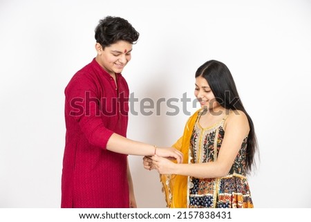Happy indian teenage girl tying rakhi on young brother's hand occasion of rakshabandha or bhi dooj isolated on white studio background. both wearing traditional festive cloths. Royalty-Free Stock Photo #2157838431