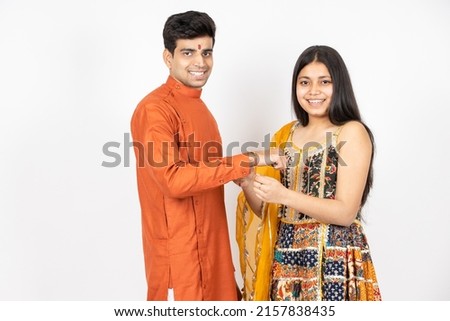 Portrait of happy indian teenage girl tying rakhi on young brother's hand occasion of rakshabandha or bhi dooj isolated on white studio background. both wearing traditional festive cloths. Royalty-Free Stock Photo #2157838435