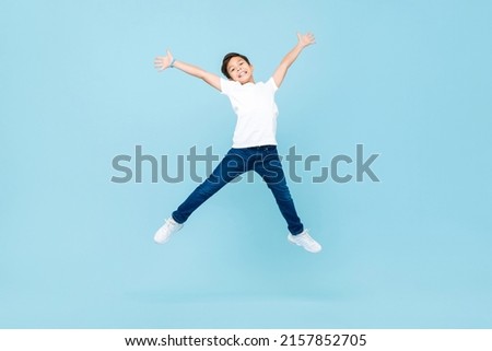 Energetic Asian mixed race boy jumping and raising hands up in isolated light blue color studio background Royalty-Free Stock Photo #2157852705