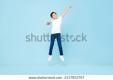 Cute Asian mixed race boy jumping with hand pointing up in isolated light blue color studio background Royalty-Free Stock Photo #2157852707