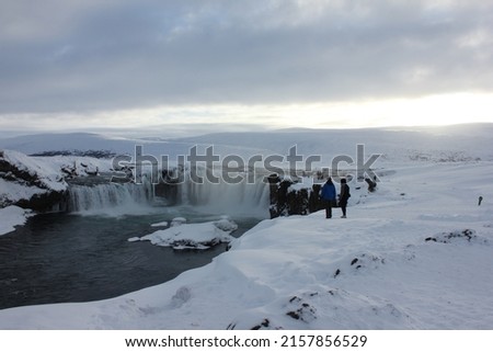 Tourists visiting the amazing Goðafoss (Godafoss) waterfall surrounded by ice and snow during a cold winter sunset in northern Iceland, Europe