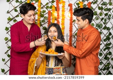 Portrait of happy indian young kids or bothers and sister wearing traditional cloths having fun eating laddu or laddoo sweets celebrating festival like diwali or rakshabandhan, Royalty-Free Stock Photo #2157859399