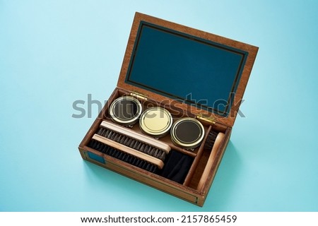 Shoe care accessories in a wooden box on blue background with copy space. Shoe shine kit with brushes, polish wax and buff cloth rag, close-up Royalty-Free Stock Photo #2157865459