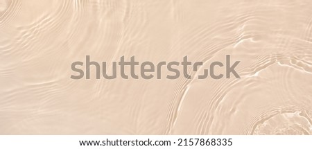 Abstract summer banner background Transparent beige clear water surface texture with ripples and splashes. Water waves in sunlight, copy space, top view. Cosmetics moisturizer micellar toner emulsion Royalty-Free Stock Photo #2157868335