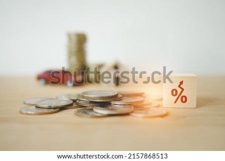 increasing percent sign on wooden cube block on pile of coins with blurred stack of coins and red miniature car