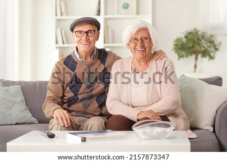Happy elderly couple sitting on a sofa at home and smiling at camera