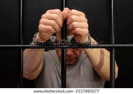 A man in handcuffs in a cell behind bars. Concept: a prisoner in a courtroom, a court sentence to a convicted person, a prison term. Royalty-Free Stock Photo #2157885077