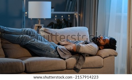Exhausted overloaded arabian man indian bearded guy unmotivated tired male came home after work flopped down on couch at night evening dark feels overworked sick ill person hard day no lack of energy