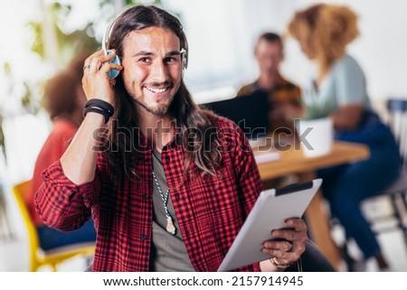Young handsome man with long hair listening music with headset and digital tablet with friends in background.