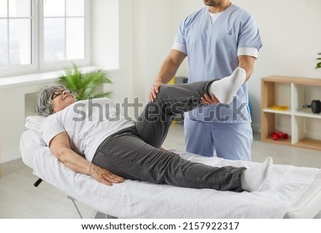 Happy senior woman lying on exam couch while chiropractor, osteopath or physiotherapy specialist is examining her leg and knee. Osteoporosis treatment, physical therapy, remedial exercise concept Royalty-Free Stock Photo #2157922317