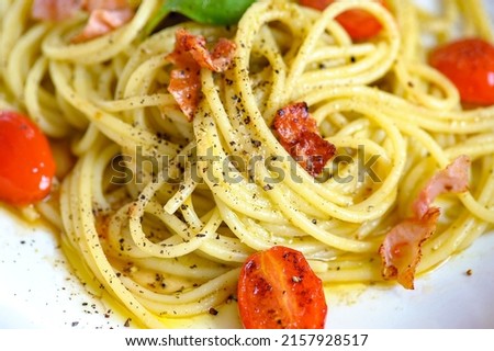 Spaghetti pasta with cherry tomatoes and bacon sprinkled with black pepper close-up