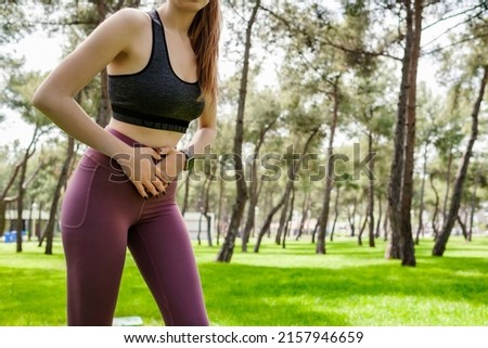Sport woman wearing sports bra and yoga pants stomachache in a city park, outdoors in summer. Beautiful young woman have stomach ache. Outdoor sports and pain concepts. Royalty-Free Stock Photo #2157946659