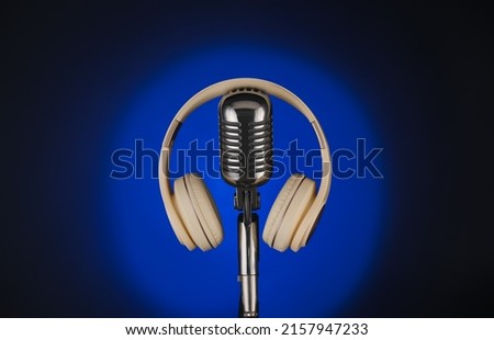 Modern microphone with headphones on dark color background, closeup