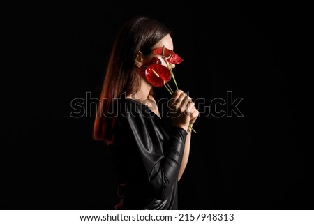 Young woman closing face with bouquet of anthurium flowers on black background