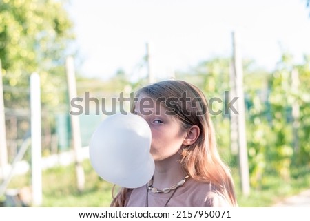 cute girl with huge chewing gum bubble in the green garden