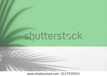 Minimal abstract background with shadow of tropical palm leaves. Presentation of cosmetic product.  Premium podium on pastel light green wall, white table. Showcase, display case, Front view. Mockup