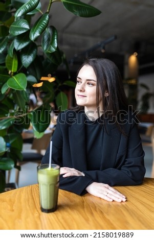 Smiling caucasian woman in a good mood drinks matcha, sits in a cafe.
Girl 20-25 years old drinks hot green tea in a glass. Royalty-Free Stock Photo #2158019889