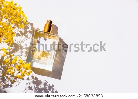 Transparent bottle of perfume with label on white background. Fragrance presentation with daylight. Trending concept in natural materials with yellow field flowers. Women's and men's essence. Royalty-Free Stock Photo #2158026853