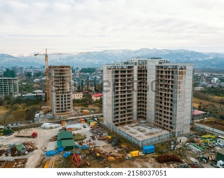 Drone view of the construction site, multi-storey buildings under construction against the background of mountains. Construction machinery, excavators, tractor crane