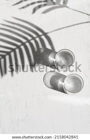 Summer white background, frame with shadow of tropical leaves and two glasses of water, minimalistic, aesthetic tropical background