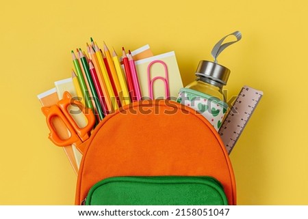 Kids Backpack with school bus on yellow background. Opened School backpack with stationery. Primary School or kindergarten.  Royalty-Free Stock Photo #2158051047