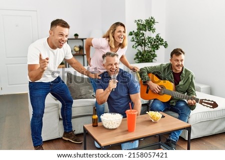 Group of middle age friends on party singing and playing guitar at home.