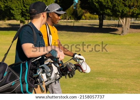 Side view of multiracial young male friends wearing caps with golf bags walking at golf course. summer, golf, unaltered, friendship, togetherness, nature, sport and weekend activities concept. Royalty-Free Stock Photo #2158057737