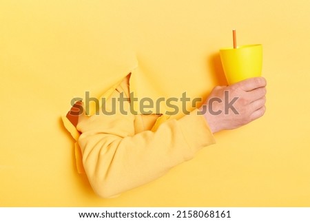 Unknown male hand holding a cup fresh cocktail, beverage in mug with straw, isolated over bright yellow background. Banner.