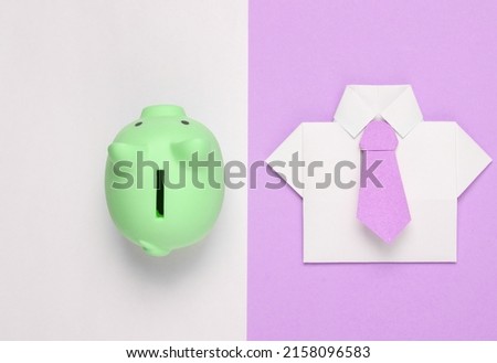 Origami paper shirt with tie, piggy bank on white pink background. Economics, Business and Finance concept