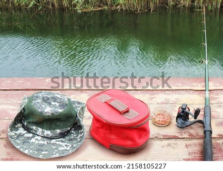 Fishing equipment, hat, fishing rod, bag, maggot bait, on the background of the lake and wildlife outdoors