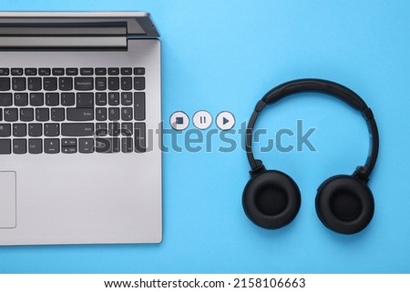 Stereo headphones and laptop with icons start, stop and pause of media player on blue background. Top view