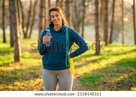 A smiling woman in sportswear poses for a photo while holding resistance strips and a bottle of water.