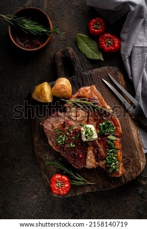 Porterhouse roast steak or Florentine beef steak with butter on a cutting board with seasonings and vegetables. Dark rustic wooden background. View from above. Royalty-Free Stock Photo #2158140719