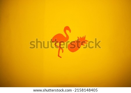 orange paper flamingo stands pineapple paper on yellow background, creative summer design