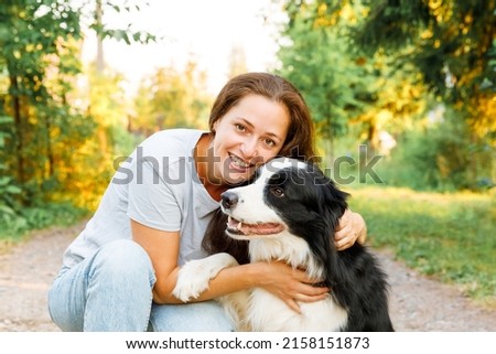 Smiling young attractive woman playing with cute puppy dog border collie on summer outdoor background. Girl holding embracing hugging dog friend. Pet care and animals concept