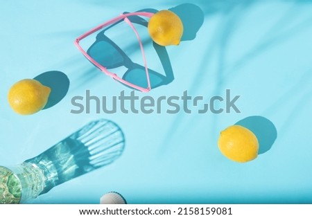 Lemons, cocktail glass, palm leaf shadows and pink color sunglasses on a light blue background. Beautiful colorful summer concept with copy space. Flat lay design.