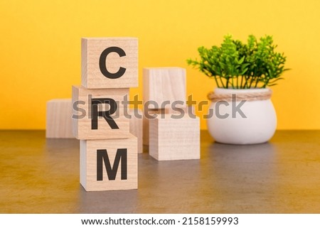 Three wooden cubes with letters - CRM on yellow table, space for text in right. front view concepts, flower in the background. CRM - Customer Relationship Management acronym
