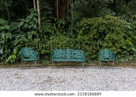 Vintage cast iron benches in green color on gravel floor and forest garden in the background, Petropolis, Rio de Janeiro, Brazil