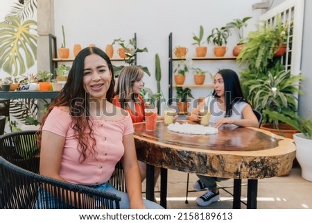 Three hispanic young adult women at a coffee shop. One is smiling and looking at the camera. Selective focus
