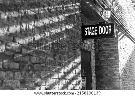 A grayscale shot of a stage door sign on a brick-walled building