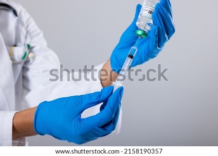 Midsection of african american mid adult female doctor wearing gloves holding vial and syringe. white background, doctor, syringe, vial, treatment, disease, hospital, healthcare, medical occupation. Royalty-Free Stock Photo #2158190357