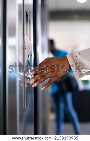 Hand of young biracial businesswoman pressing elevator button at modern workplace. unaltered, business, modern office, convenience and technology concept.