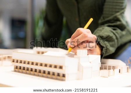 Midsection of caucasian female architect examining model with pencil at modern workplace. unaltered, creative business and modern office concept.
