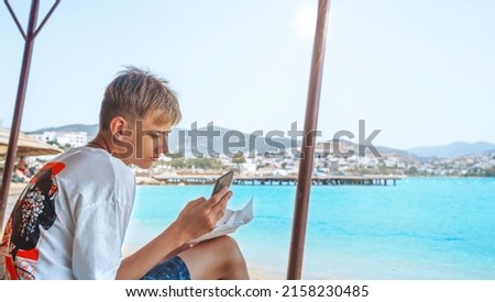 Handsome white teenager with modern mobile smart phone on the beach in Bodrum city Turkey. Close-up