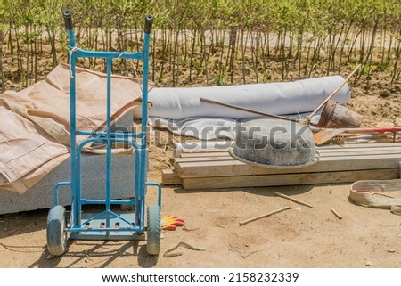 Blue metal hand truck with miscellaneous tools at construction site. Royalty-Free Stock Photo #2158232339