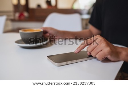 Closeup image of a woman using and touching on mobile phone screen while drinking coffee in cafe