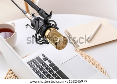 Stand with professional microphone, cup of tea and laptop on light table in room